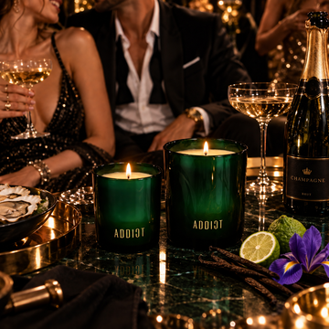 ADDICT Revelry luxury soy candles, lit, on a marble table with champagne glasses at an evening celebration